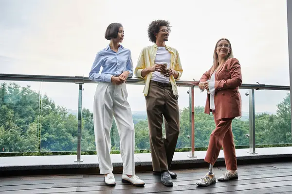 Three colleagues, diverse in race and ability, enjoy a casual conversation on an office rooftop terrace. — Stock Photo