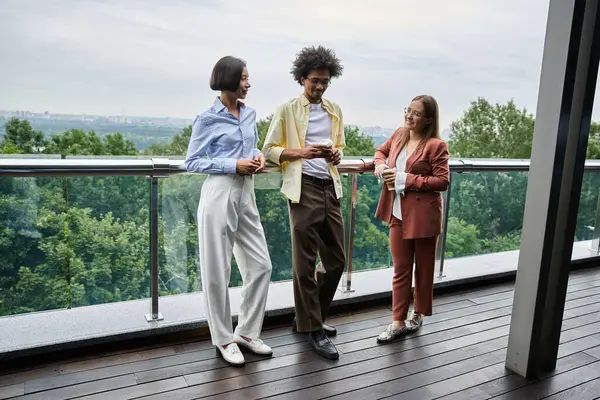 Three colleagues chat and laugh on a modern rooftop terrace. — Stock Photo