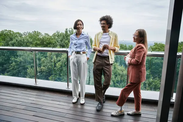 Three colleagues chat on a rooftop terrace, enjoying a break in their workday. — Stock Photo