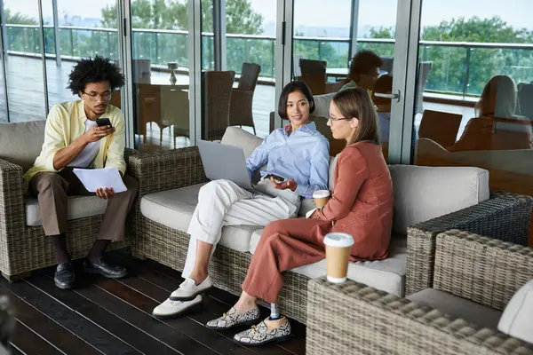 Three colleagues, diverse in race and ability, engage in conversation and work on a rooftop terrace. — Stock Photo