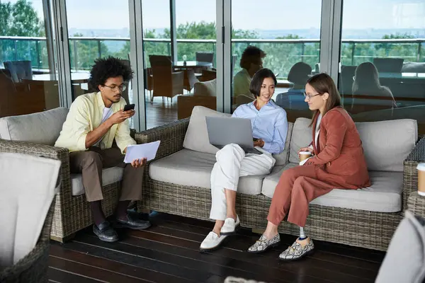 Diverse colleagues enjoy a break on a modern office rooftop terrace, engaging in conversation and work. — Stock Photo