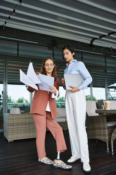 Two colleagues, one with a prosthetic leg, stand on a rooftop terrace, reviewing documents and chatting. — Stock Photo