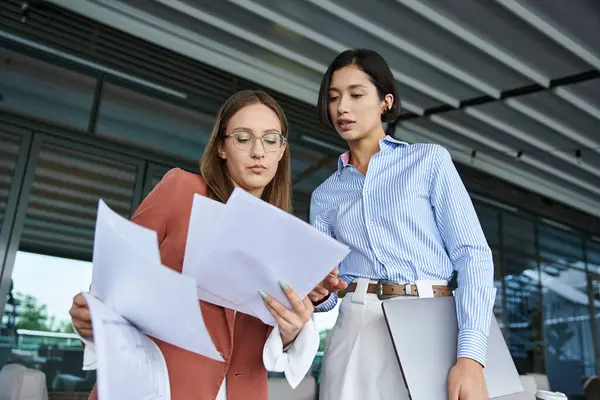 Two colleagues, one with a prosthetic leg, review paperwork while standing on a rooftop terrace. — Stock Photo