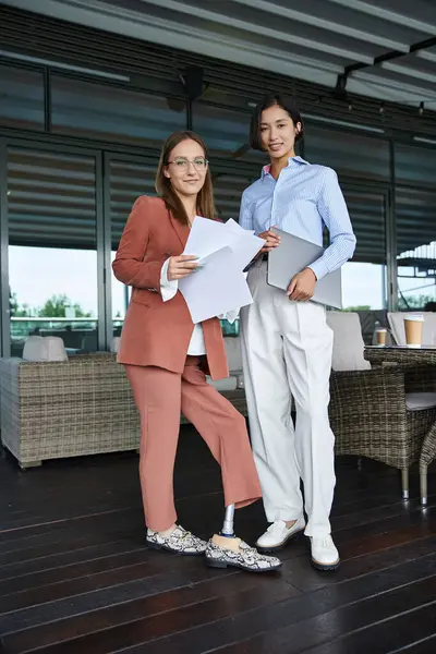 Two colleagues, one with a prosthetic leg, stand on a rooftop terrace, chatting and reviewing documents. — Stock Photo