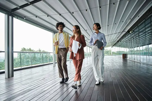Three colleagues, including a woman with a prosthetic leg, walk and chat on a modern rooftop terrace. — Stock Photo