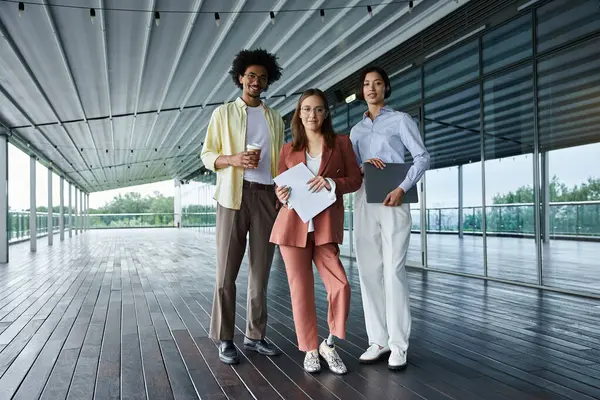 Three diverse colleagues chat and work on a rooftop terrace. — Stock Photo