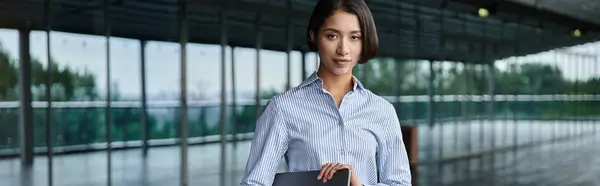 An asian woman stands on a modern rooftop terrace, holding a laptop in her hands. — Stock Photo