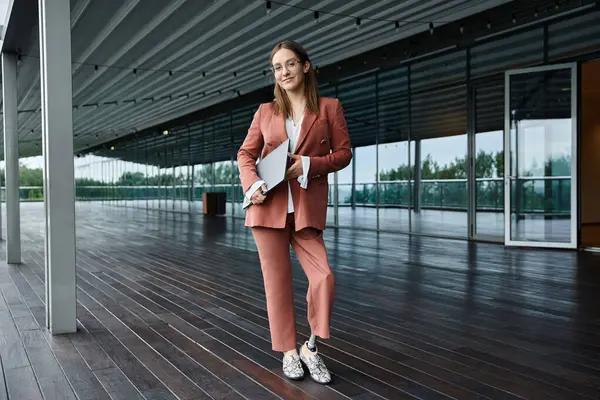 Eine Frau im roten Anzug steht selbstbewusst auf einer Dachterrasse, einen Laptop in der Hand, mit Beinprothese. — Stockfoto