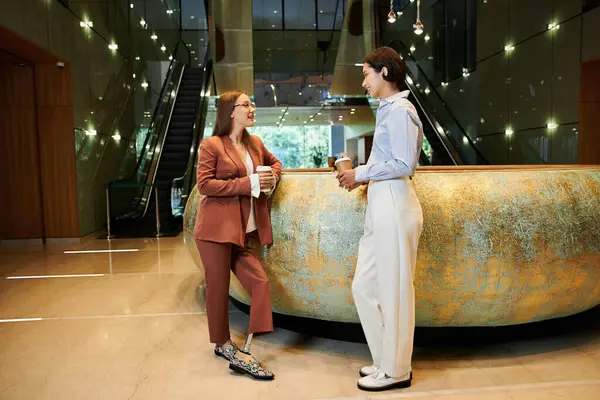 Two colleagues, one with a prosthetic leg, chat and enjoy coffee in a modern office lobby. — Stock Photo