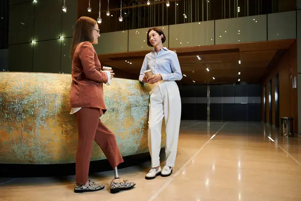 Two colleagues chat and enjoy coffee in the office lobby, showcasing diversity and inclusivity. — Stock Photo