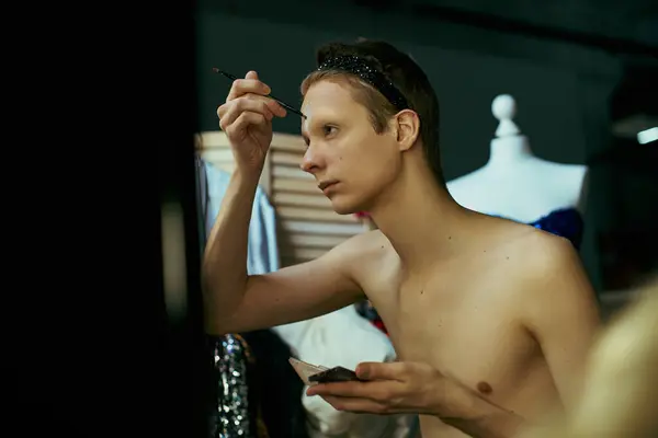 A drag queen applies makeup to their face while looking into a mirror in a dimly lit backstage area. — Stock Photo