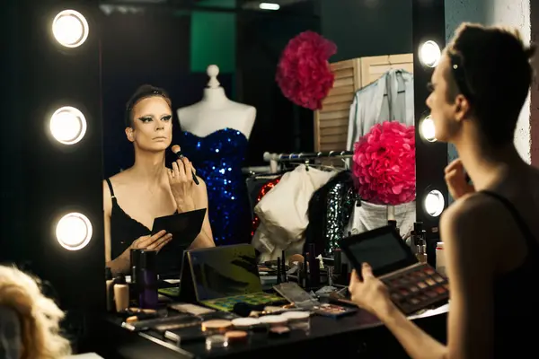 Uma drag queen aplica maquiagem enquanto olha em um espelho nos bastidores. — Fotografia de Stock