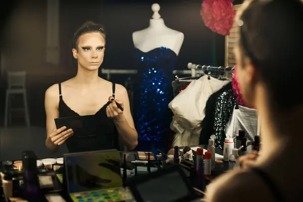 Un drag performer aplica maquillaje delante de un espejo, rodeado de cosas entre bastidores — Stock Photo