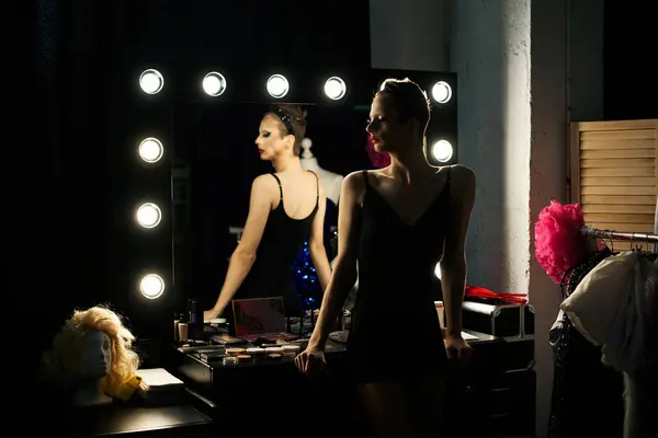 A drag queen stands near a vanity with a lit-up mirror, preparing for a performance. — Stock Photo