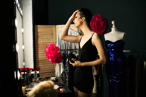 A drag queen adjusts her hair and makeup before taking the stage, looking in the mirror surrounded by various costumes. — Stock Photo