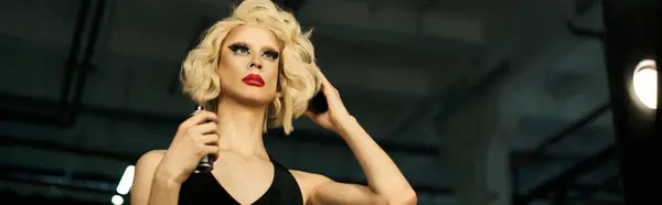 A drag queen with bright makeup and a glamorous blonde wig, gets ready backstage, adjusting her hair and spraying perfume. — Stock Photo