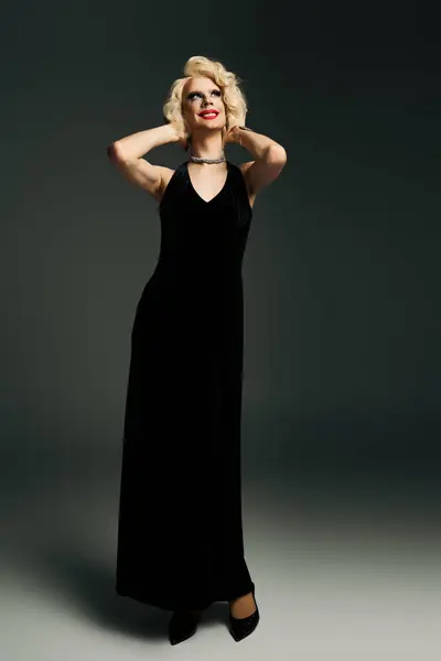 A drag queen with dramatic makeup, a blonde wig, and a long black dress poses against a gray backdrop. — Stock Photo
