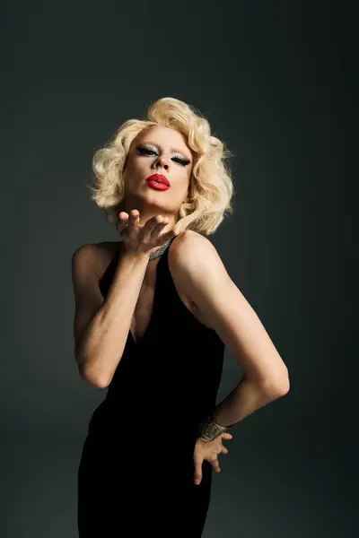 Una drag queen in un abito nero e parrucca bionda soffia un bacio alla fotocamera. — Foto stock