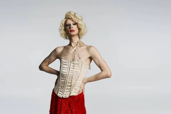 A drag queen in a blonde wig, red skirt, and white corset poses against a grey backdrop. — Stock Photo