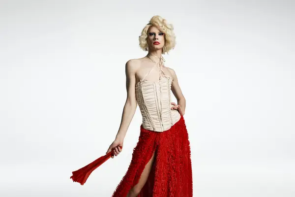 A drag queen in a blonde wig poses in a red skirt and white corset against a grey backdrop. — Stock Photo