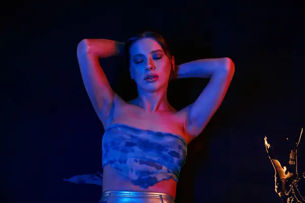 A young woman in a trendy crop top poses by the poolside, bathed in neon blue light. — Stock Photo