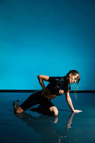 Uma mulher em um top de cultura de látex preto e shorts posa em uma superfície refletiva azul, criando uma imagem cativante. — Fotografia de Stock