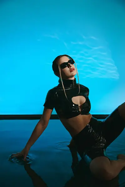 A young woman poses in a black latex crop top and shorts, her hand reaching into the water in front of her. — Stock Photo