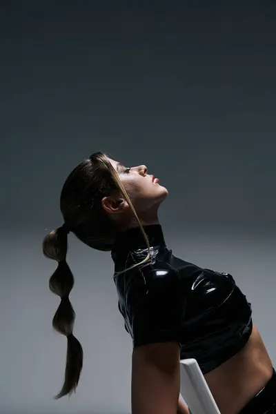 Una giovane donna in un crop top nero posa su uno sfondo grigio. I suoi capelli in una coda di cavallo elegante aggiunge al look contemporaneo — Foto stock