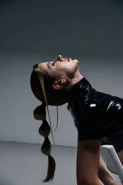 Una donna in lattice nero crop top posa su uno sfondo grigio, i capelli in stile coda di cavallo lunga. — Foto stock