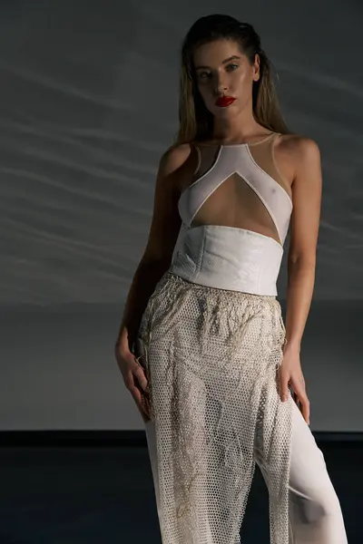 A young woman in a white outfit, featuring a mesh skirt and a fitted top, poses confidently against a grey backdrop. — Stock Photo