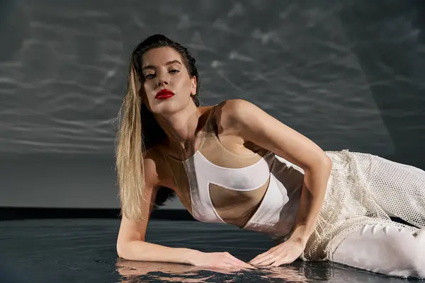 A young woman in white poses against a grey background, hair flowing and eyes locked on the camera — Stock Photo