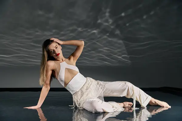 A young woman in a white outfit poses on a grey background, with water reflections cast above her. — Stock Photo