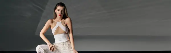 A young woman in a white outfit poses against a grey backdrop, showcasing a trendy style. — Stock Photo