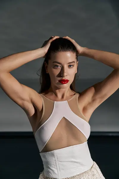 A young woman with long dark hair and red lipstick poses against a gray backdrop, wearing a white top and skirt. — Stock Photo