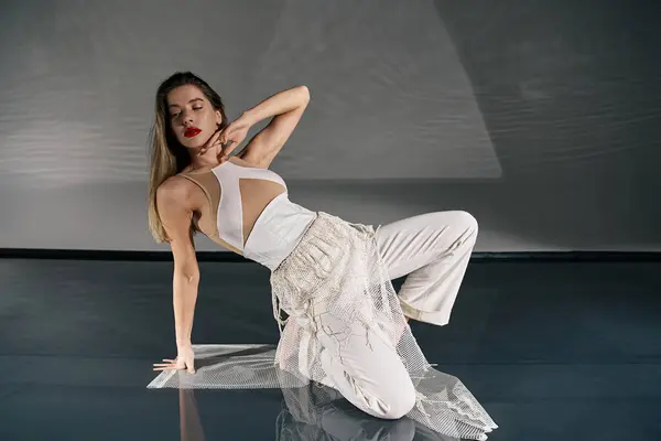 A young woman in a white outfit poses gracefully on a grey backdrop, her long hair cascading around her shoulders. — Stock Photo
