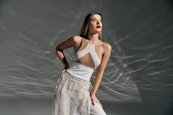 A young woman in a white outfit poses against a grey backdrop, her long hair flowing and her gaze directed upwards. — Stock Photo