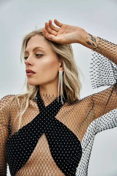A young blonde woman poses in a black fishnet swimsuit against a grey background. — Stock Photo
