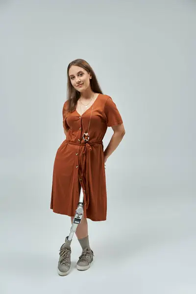 Woman in rust dress and prosthetic leg poses against white backdrop, smiling confidently at camera — Stock Photo