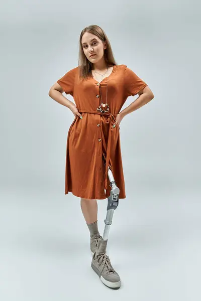 A woman stands confidently in a rust-colored dress with a prosthetic leg. — Stock Photo