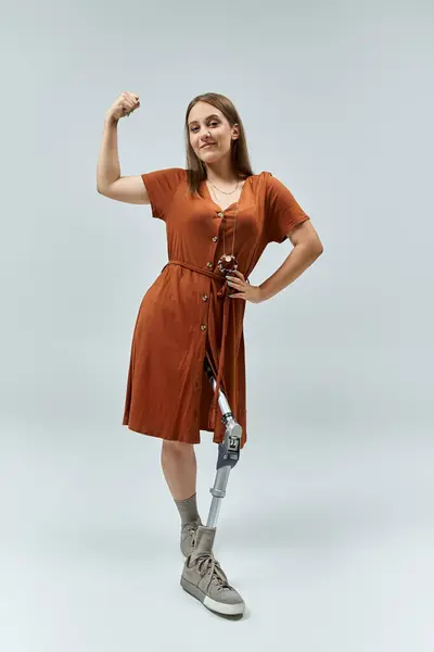 A woman in a brown dress stands with her arm raised, confidently displaying her prosthetic leg. — Stock Photo