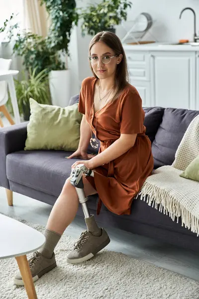 A woman in a brown dress sits on a couch, confidently looking at the camera. — Stock Photo