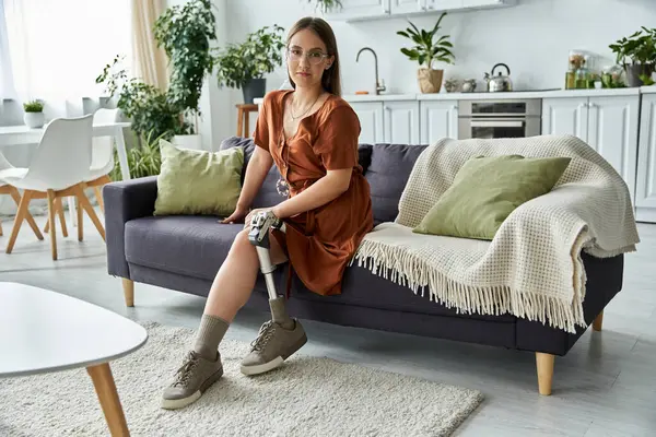 A woman with prosthetic leg sits on a couch. — Stock Photo