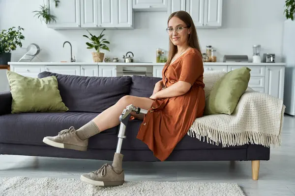 A woman with a prosthetic leg sits on a couch, looking confidently at the camera. — Stock Photo