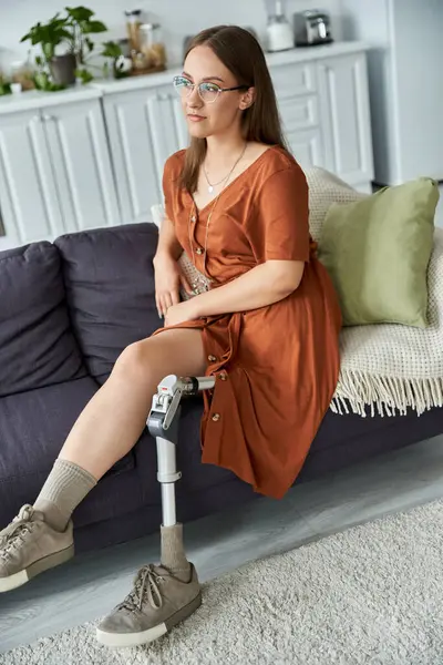 A young woman with a prosthetic leg sits confidently on a sofa in her living room. — Stock Photo