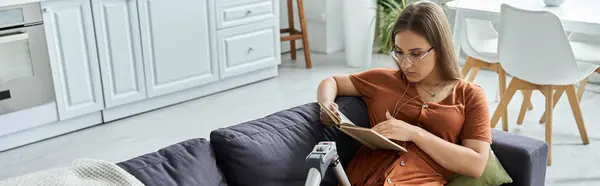 Uma mulher com uma perna protética senta-se em um sofá, absorvido na leitura de um livro. — Fotografia de Stock