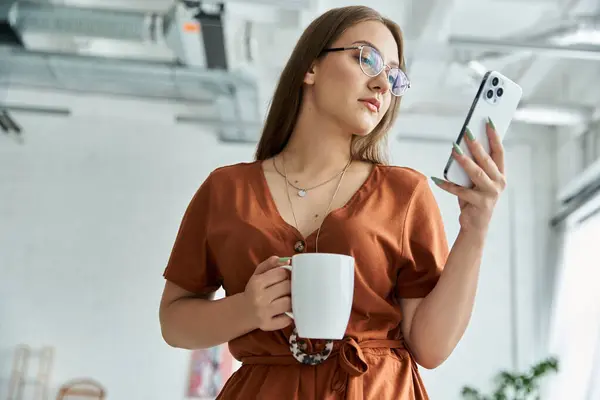 Woman texts and holds coffee cup in bright room — Stock Photo