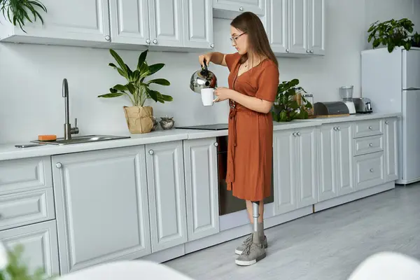 Una mujer con una pierna protésica vierte café en su cocina. - foto de stock