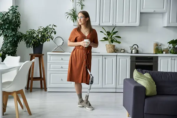 Mujer en vestido marrón se para en la cocina moderna, sosteniendo taza, mirando cuidadosamente por la ventana — Stock Photo