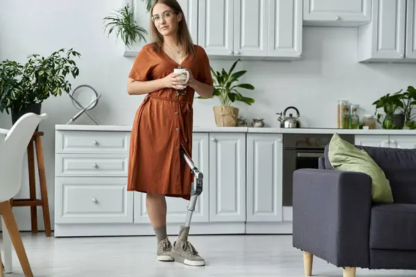 A woman in a brown dress stands in a kitchen holding a cup of coffee. — Stock Photo