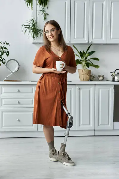 A woman with a prosthetic leg holds a cup of coffee in a modern kitchen. — Stock Photo